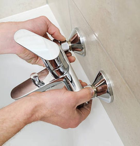 Plumber holding a bath tub faucet and installs it.